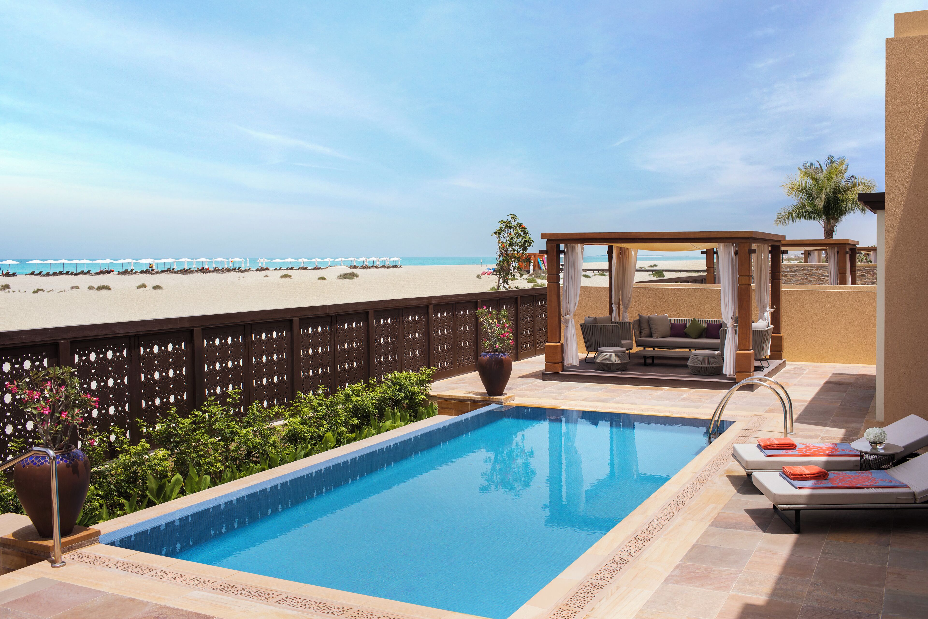 Una piscina en la azotea con vista a la playa, un área de estar techada y una palmera.