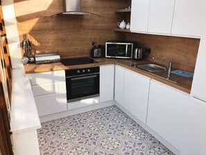 A compact kitchen with white cabinets, a microwave, a stove, and a sink. - Hookless Holiday Homes (Templetown)