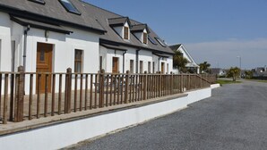 A row of white buildings with wooden doors and windows, a gravel driveway, and a wooden fence. - Hookless Holiday Homes (Templetown)