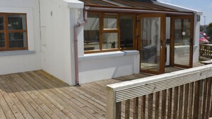 A building with a wooden deck, a covered patio area, and a glass door leading to an interior space. - Hookless Holiday Homes (Templetown)