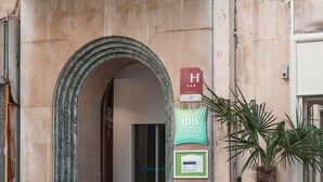 A hotel entrance with a stone archway, a sign for ibis Styles Hotels, and a palm plant beside the door. - Hôtel Ibis Styles Marseille Vieux Port (Marseille)
