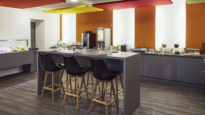 A modern kitchen with a central island, bar stools, a coffee machine, and a refrigerator. - Hôtel Ibis Styles Marseille Vieux Port (Marseille)