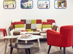 A cozy room with a colorful patchwork sofa, a red armchair, a small white table, and a magazine. - Hôtel Ibis Styles Marseille Vieux Port (Marseille)