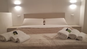 Un lit bien fait, avec des draps blancs, deux oreillers et une couverture beige. Deux serviettes enroulées sont posées sur le lit.