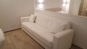 Un canapé blanc, avec un miroir au-dessus, un plancher en bois et un interrupteur sur le mur.