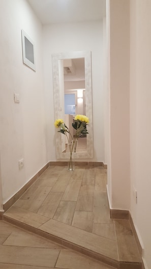 A hallway with a tiled floor, a door, and a mirror reflecting a room with a blue door.