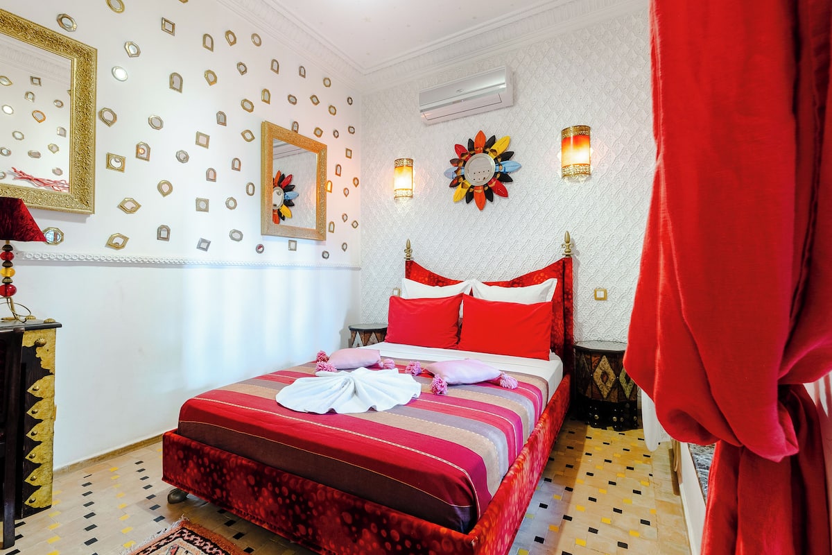 Une chambre d’hôtel avec un lit, un miroir, des décorations murales et un rideau rouge.