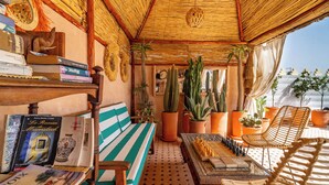 A cozy reading nook with a striped bench, a chessboard, and a variety of books and decorative items. - Riad Asrari  (Marrakech)