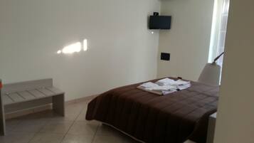 Un dormitorio con cama, un banco, un televisor montado en la pared y un equipo de aire acondicionado.