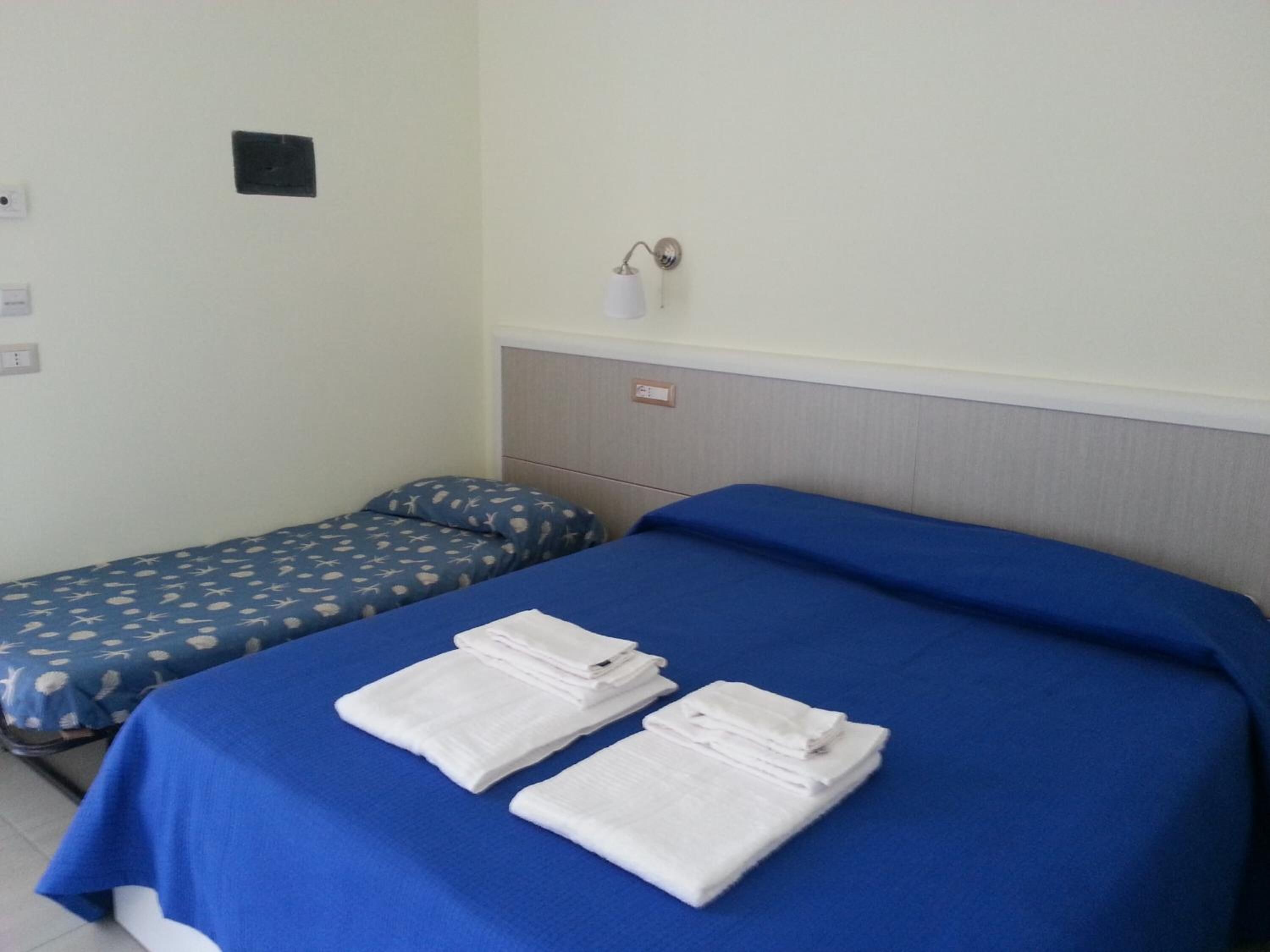 A hotel room with two beds, each with a blue bedspread and white linens.
