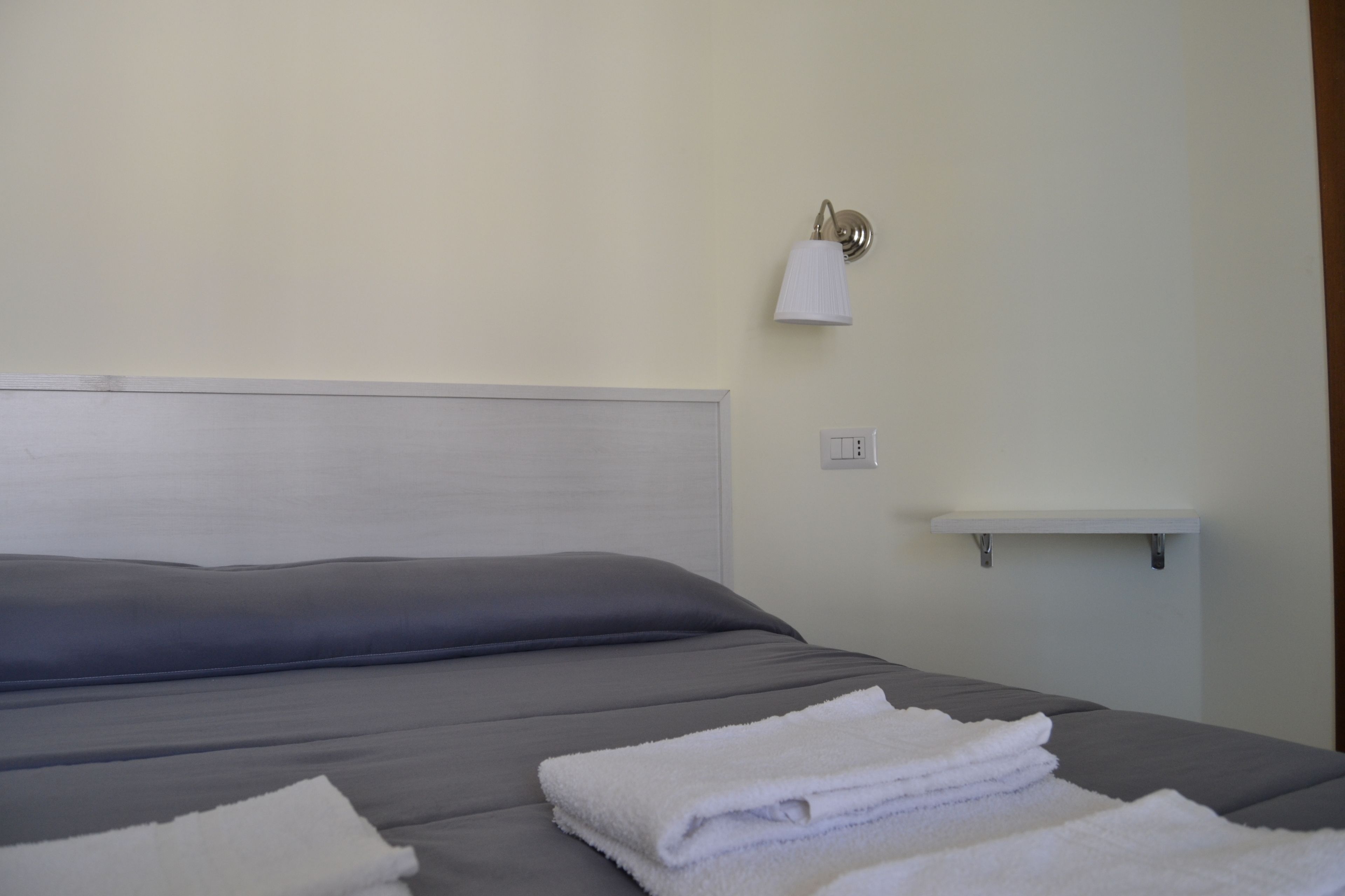Un lit bien fait, avec une tête de lit grise et des serviettes blanches posées dessus.