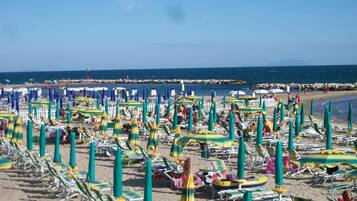 Une plage bordée de rangées de chaises longues et de parasols, une digue rocheuse en arrière-plan et l’océan.