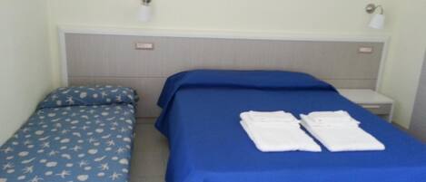 A room with two beds, one with a blue bedspread and the other with a blue bedspread with a white pattern. There are two white towels on the larger bed.