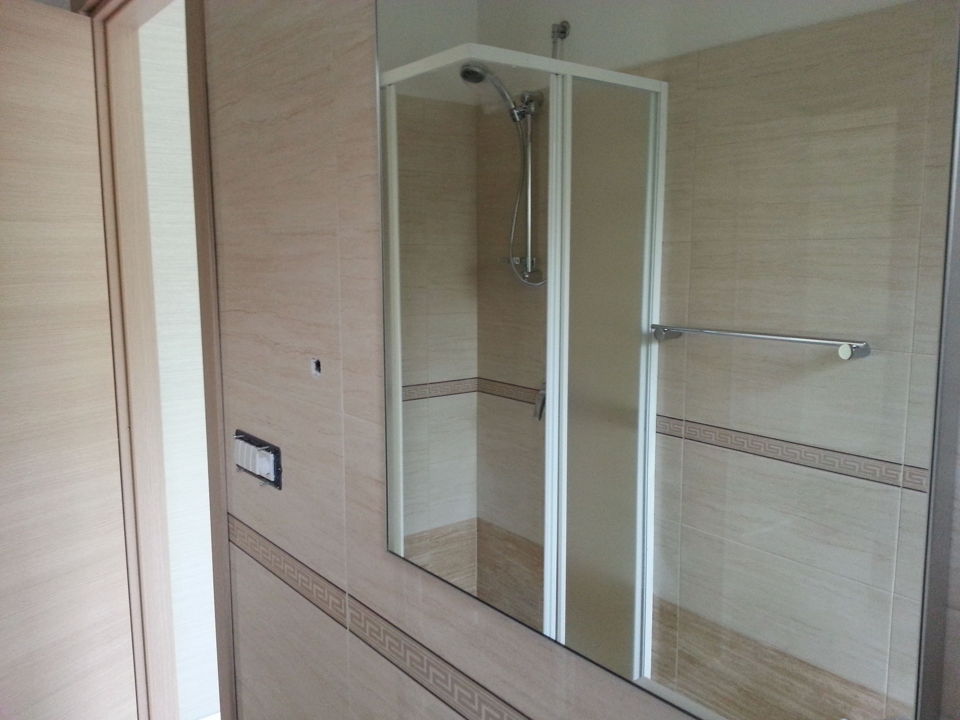 A shower with a glass door, a towel rack, and a light switch on the wall.
