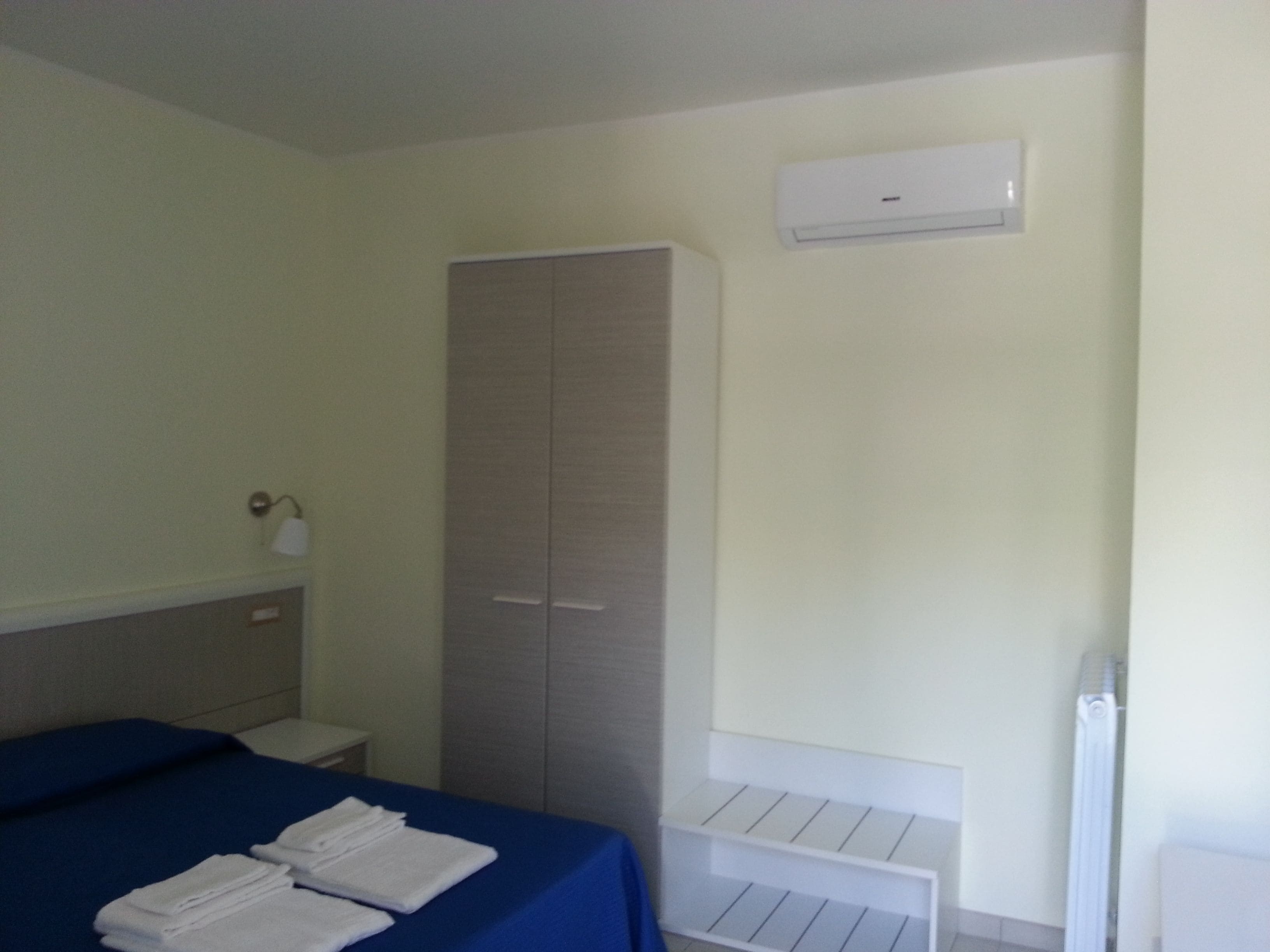 A hotel room with a bed, a wardrobe, a bedside table, and a radiator.