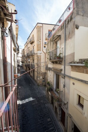 Une ruelle étroite entre deux immeubles dotés de balcons, un chemin pavé et des tuyaux et des câbles apparents.