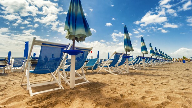 Una playa con filas de sillas azules y sombrillas a juego.