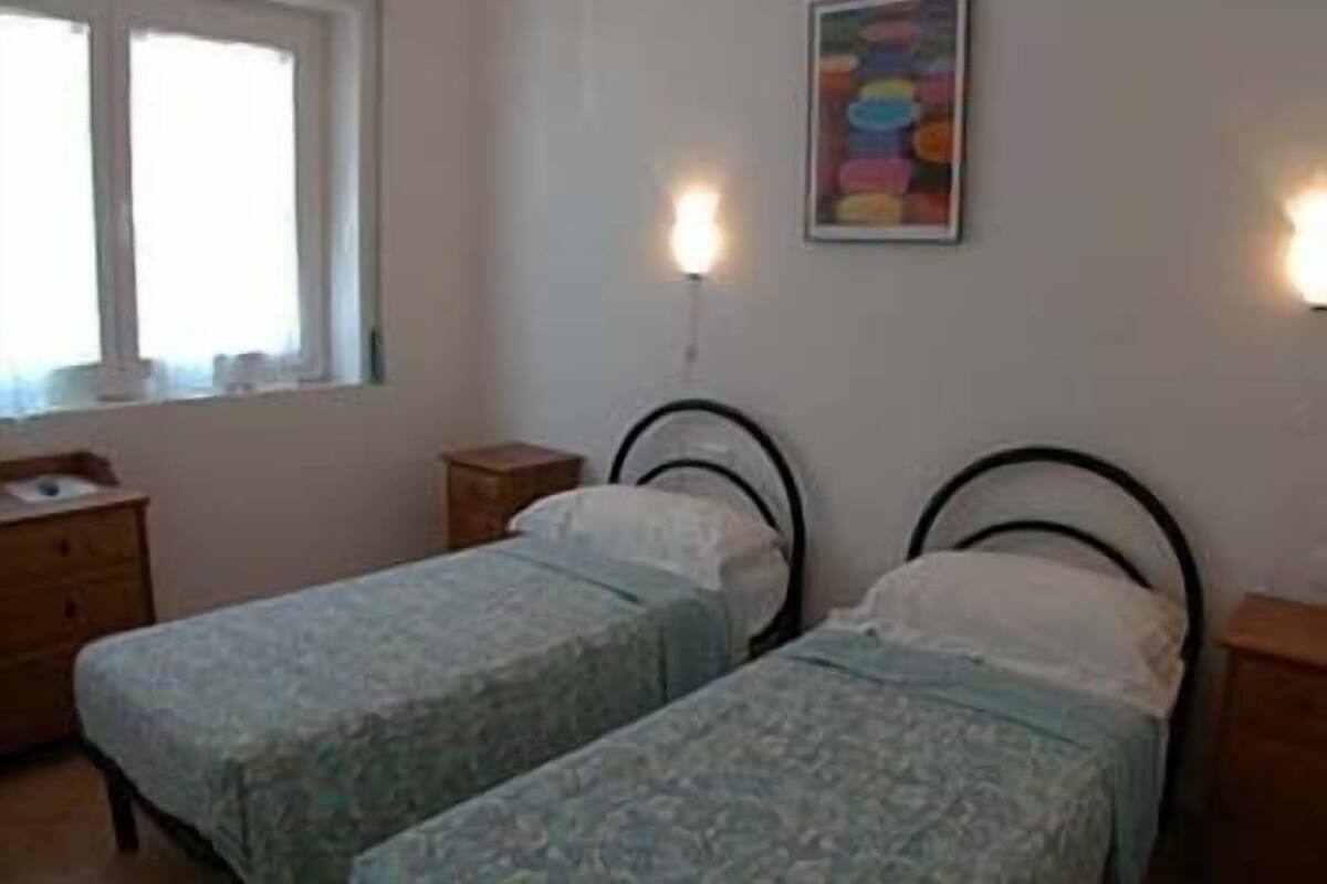 A bedroom with two single beds, a bedside table, a dresser, and a window.