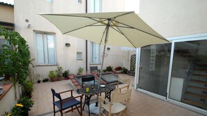 Un patio al aire libre con mesa y sillas, una sombrilla grande y plantas en macetas.