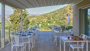 Terraza exterior con mesas y sillas, con vistas a un paisaje montañoso.