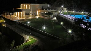 Una casa moderna de dos pisos con piscina, iluminada con varias luces.