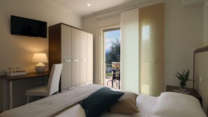 Habitación de hotel con cama, escritorio con lámpara, televisor y vistas al exterior.