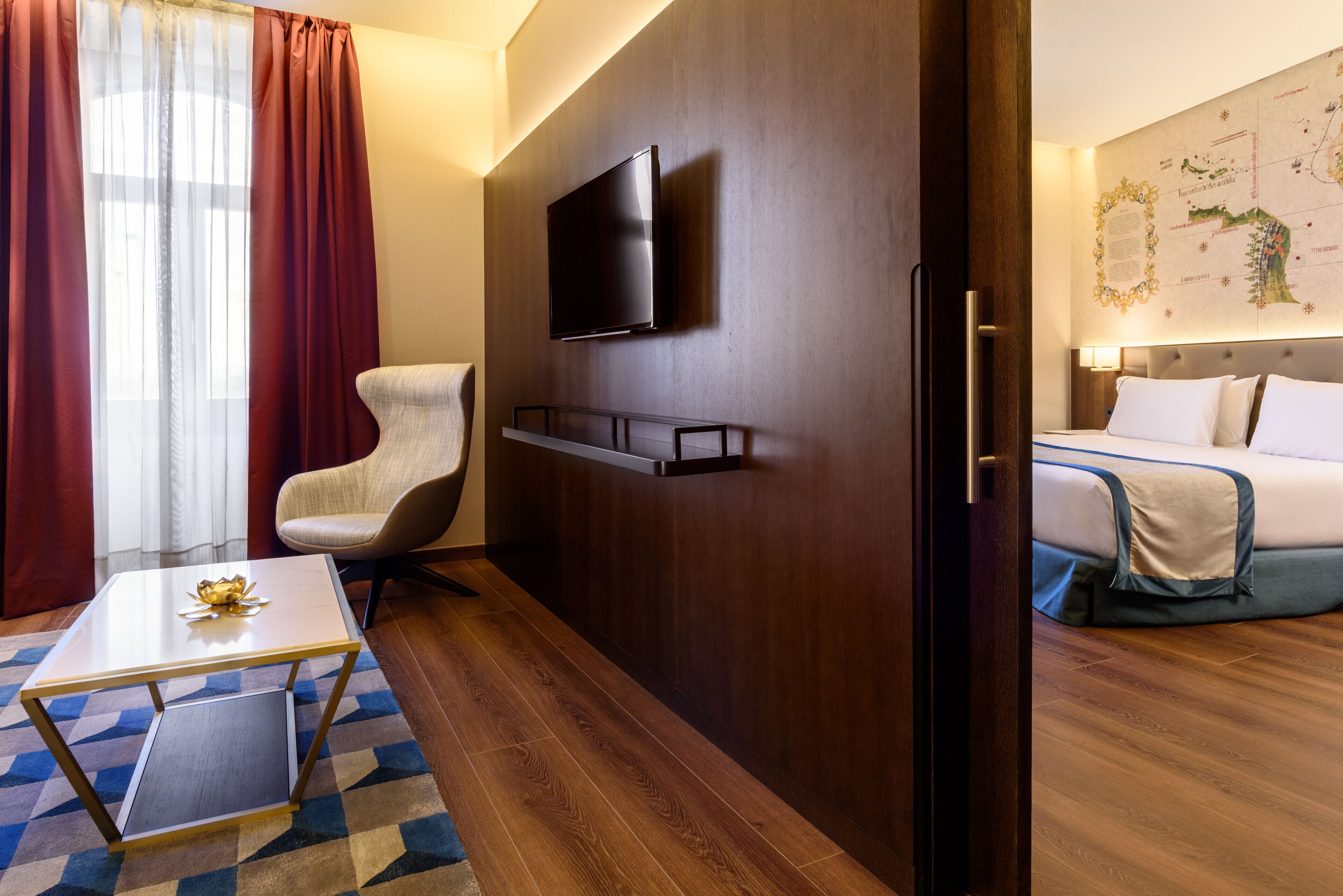 Une chambre d’hôtel avec un lit, un téléviseur fixé au mur, une chaise, une petite table et une carte accrochée au mur.
