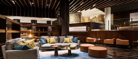 A modern lobby with a sofa set, round coffee table, and ottoman, a stone wall, and a reception desk.