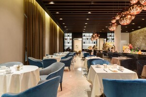Ein Restaurant mit runden Tischen und blauen Stühlen, einer Holzwand und einer Kronleuchter.