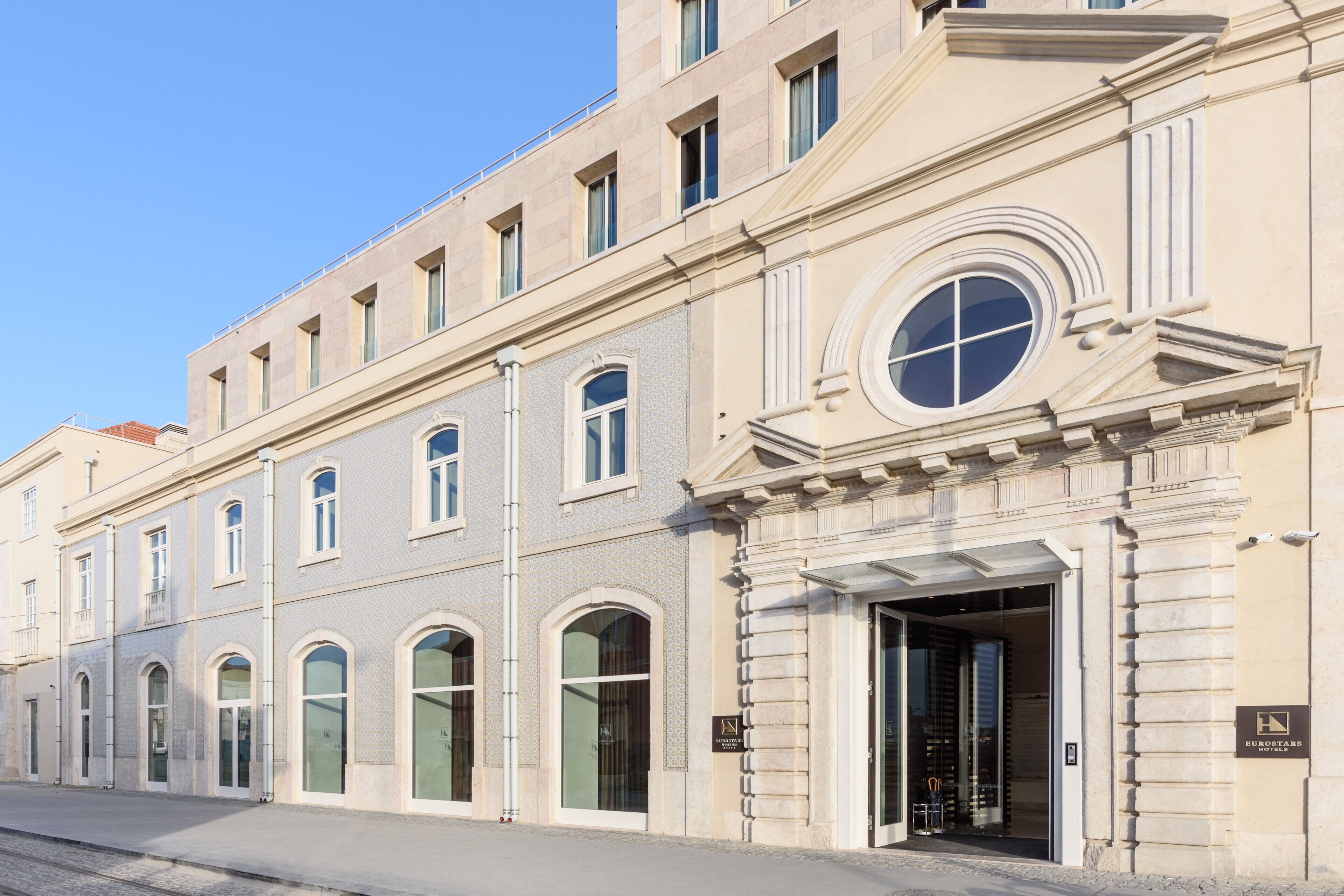 Un bâtiment historique à la façade classique, doté de grandes fenêtres en arc de cercle et d’une entrée imposante avec une porte en verre.