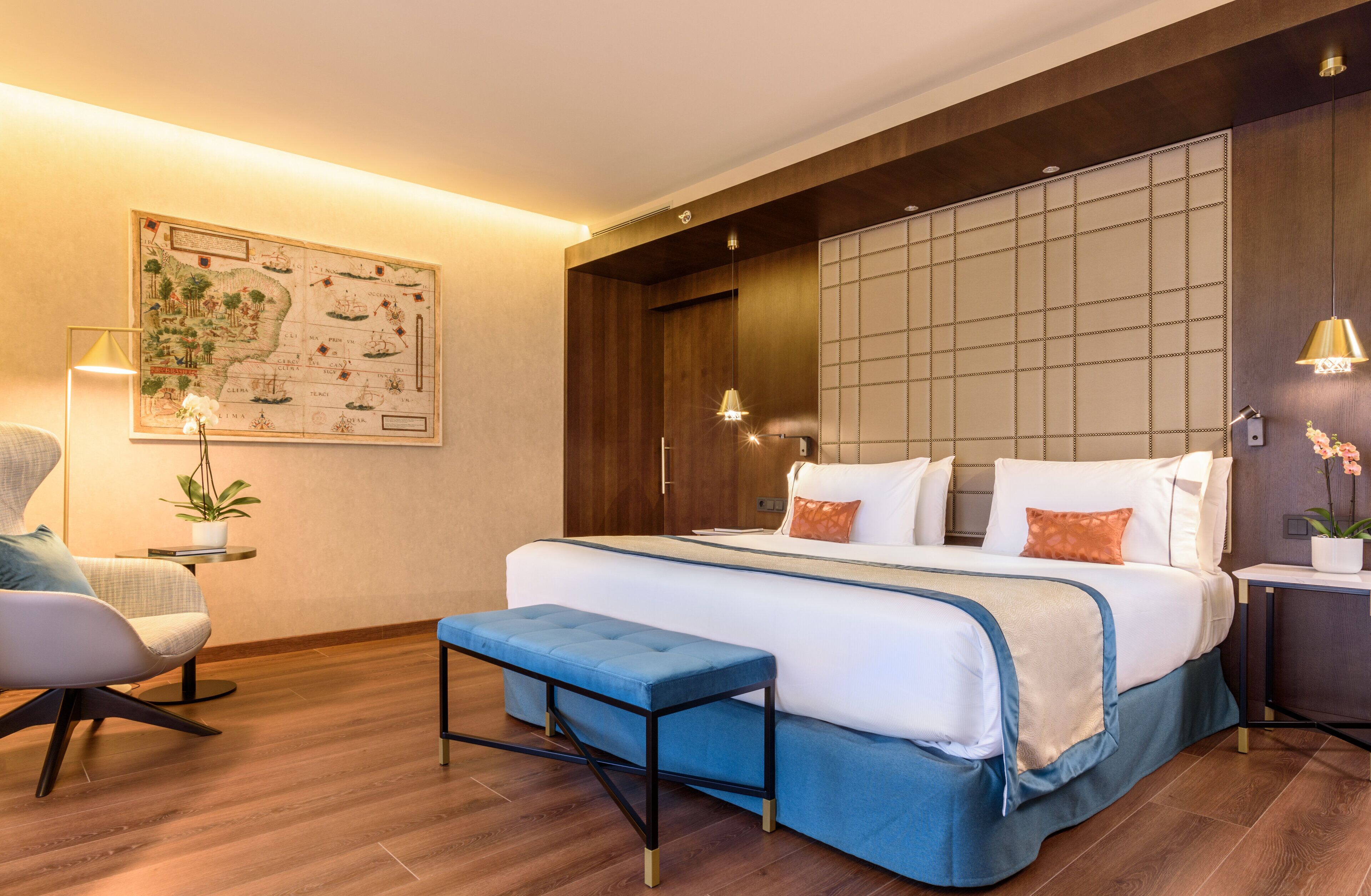 A modern bedroom with a large bed, a bench, a chair, and a map on the wall.