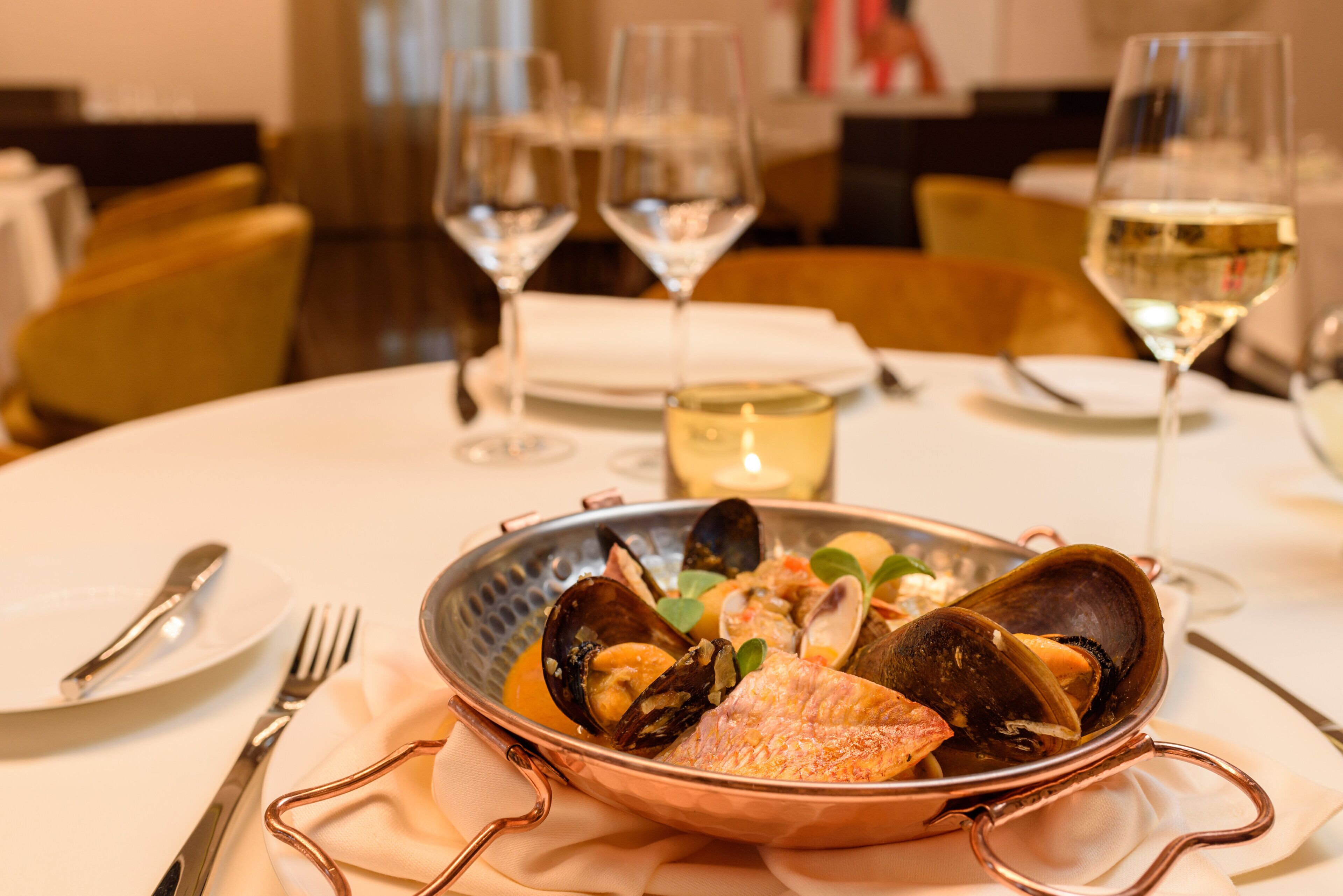 A dining table with a seafood dish, wine glasses, and cutlery.