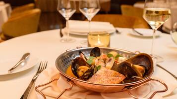 A dining table with a seafood dish, wine glasses, and cutlery.