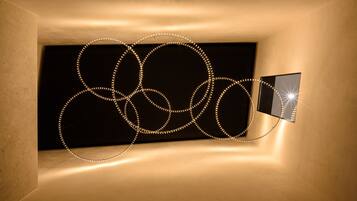 A room with a unique light installation on the wall, a framed picture, and a textured wall.