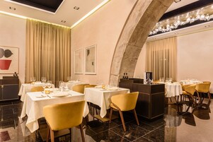 A restaurant with tables set for dining, featuring a modern interior with a stone archway and a chandelier.
