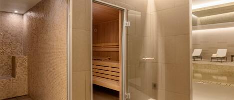 Un baño moderno con cabina de ducha de vidrio, sauna de madera y zona de estar con sillas.