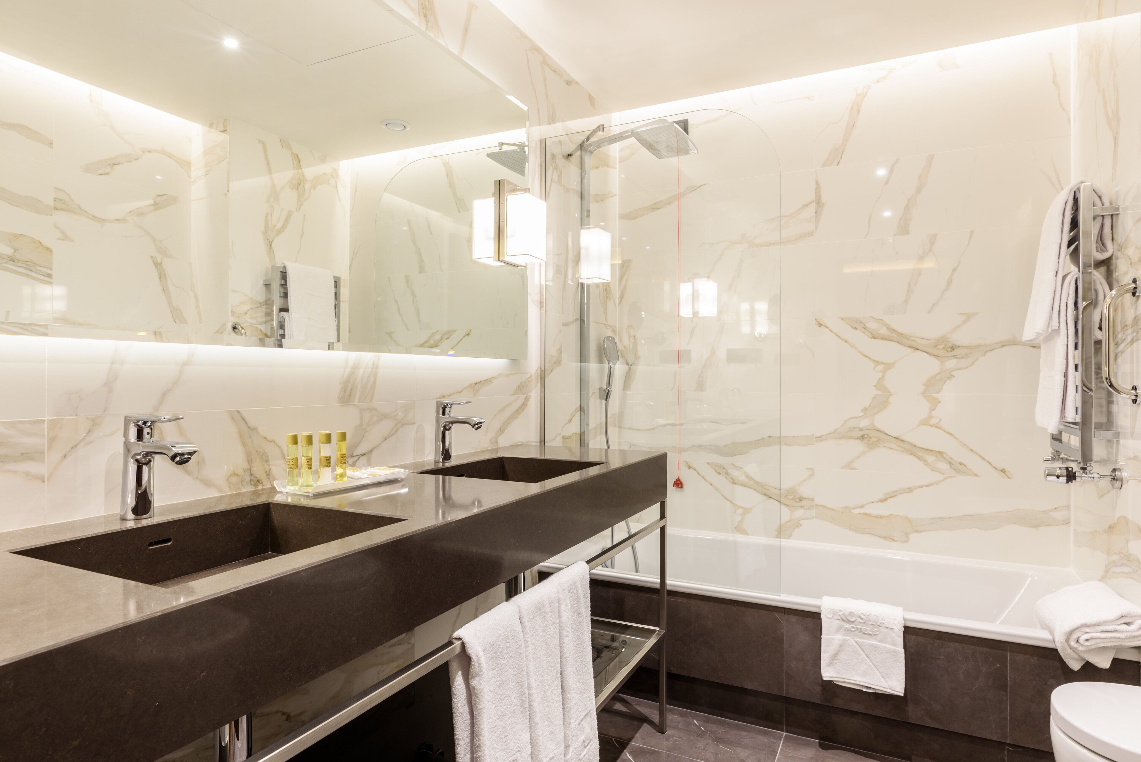 A modern bathroom with two sinks, a large mirror, and a bathtub.