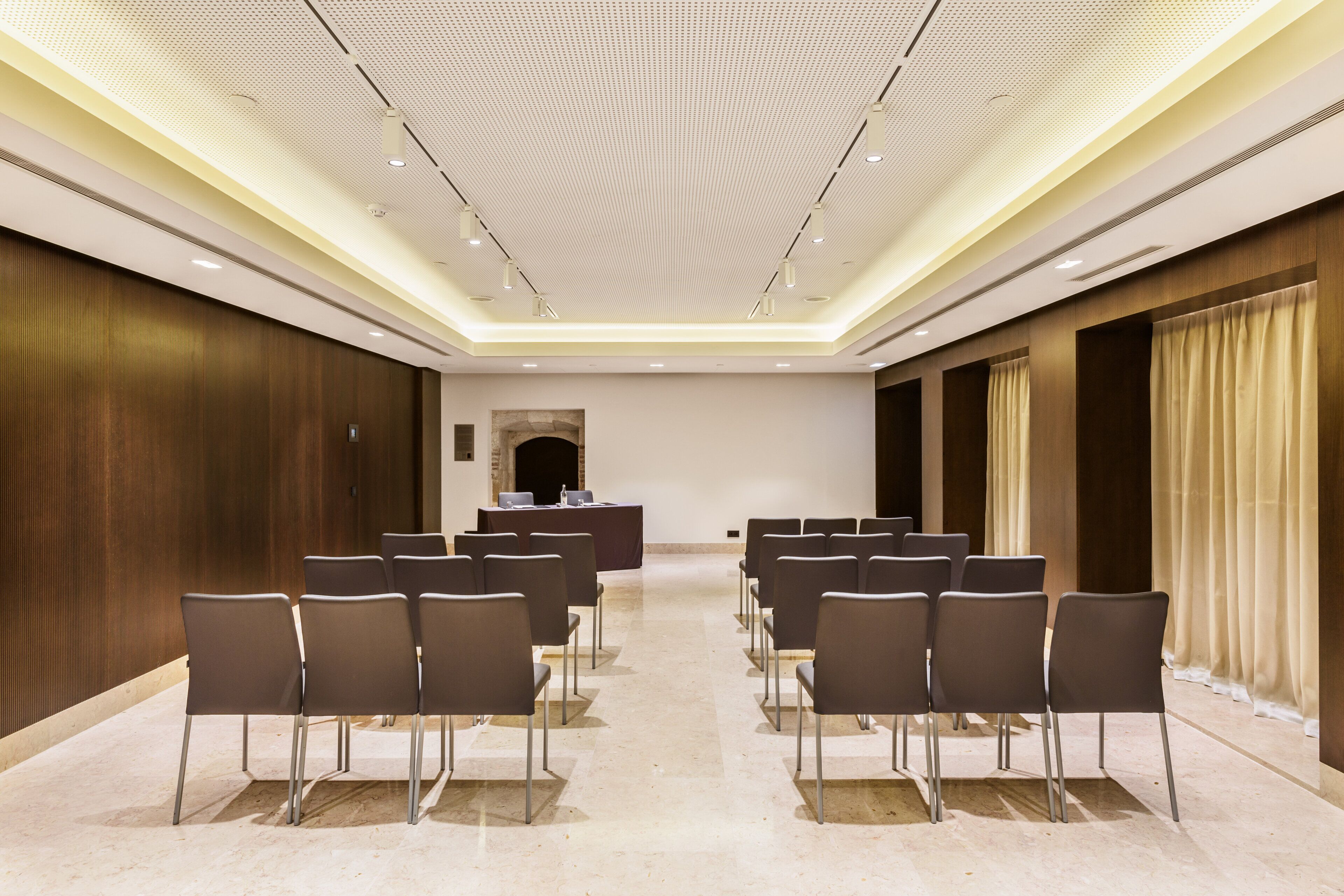 Un salón de conferencias con filas de sillas, un atril y un techo alto con iluminación empotrada.