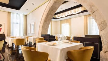 A restaurant with round tables, yellow chairs, and stone arches.