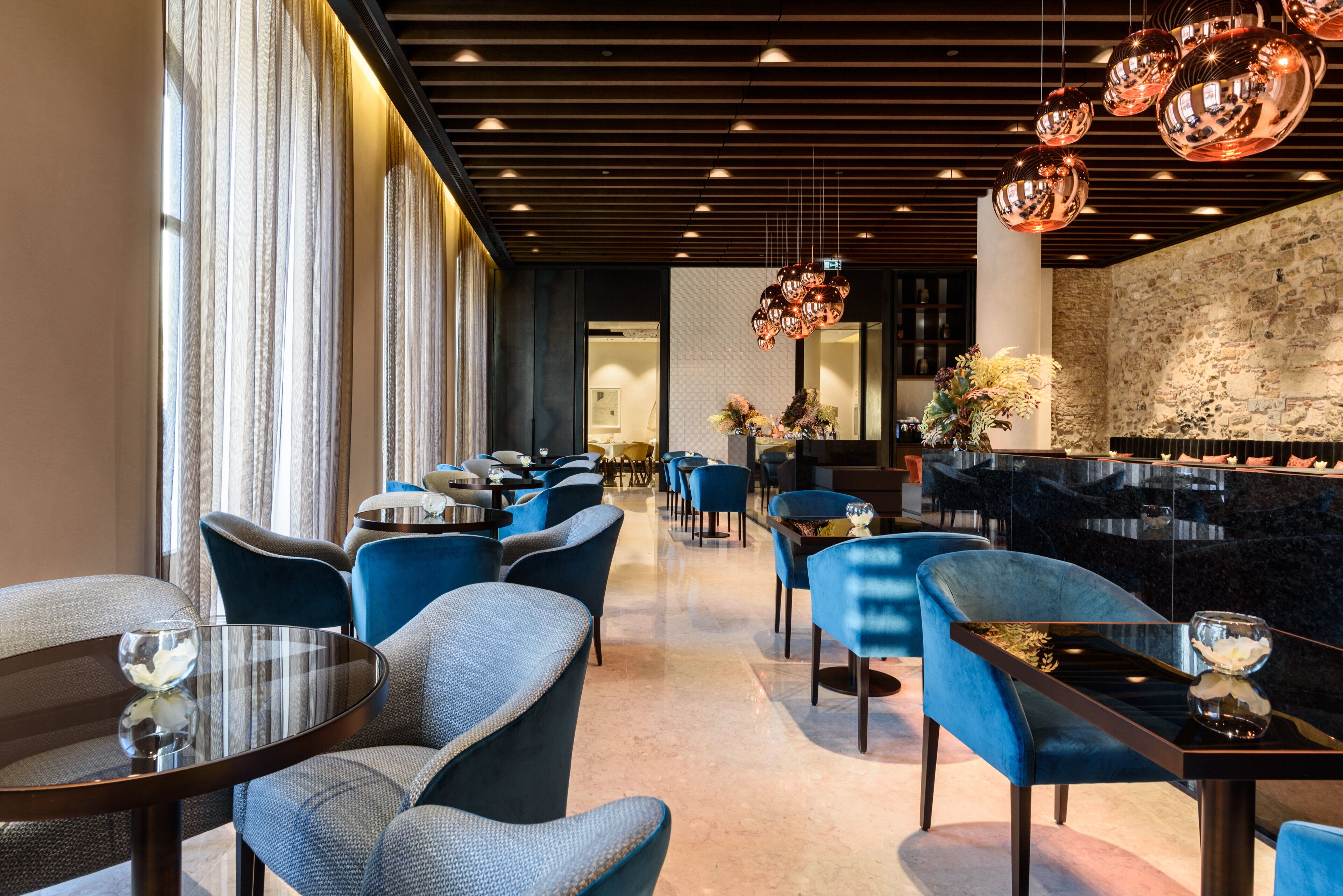A modern restaurant with blue upholstered chairs, round tables, and a black marble bar area.