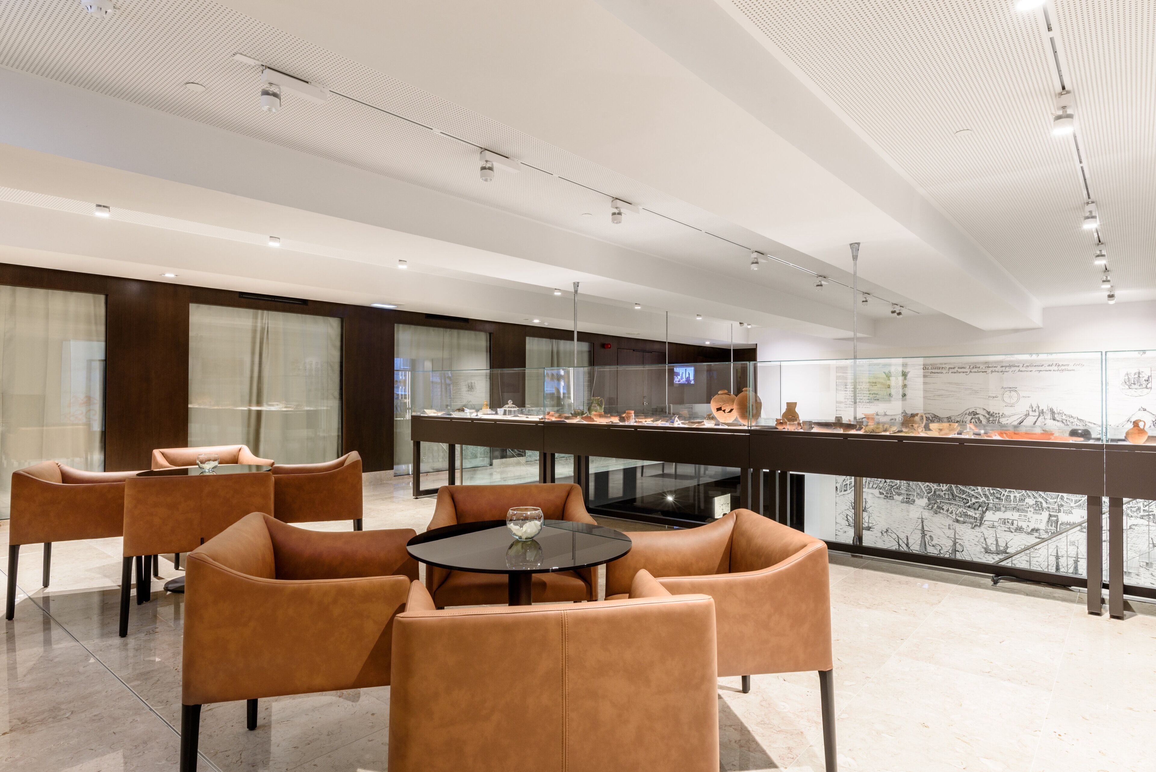 Un interior moderno con sillones de cuero, una mesa con superficie de vidrio y una vitrina con artefactos.