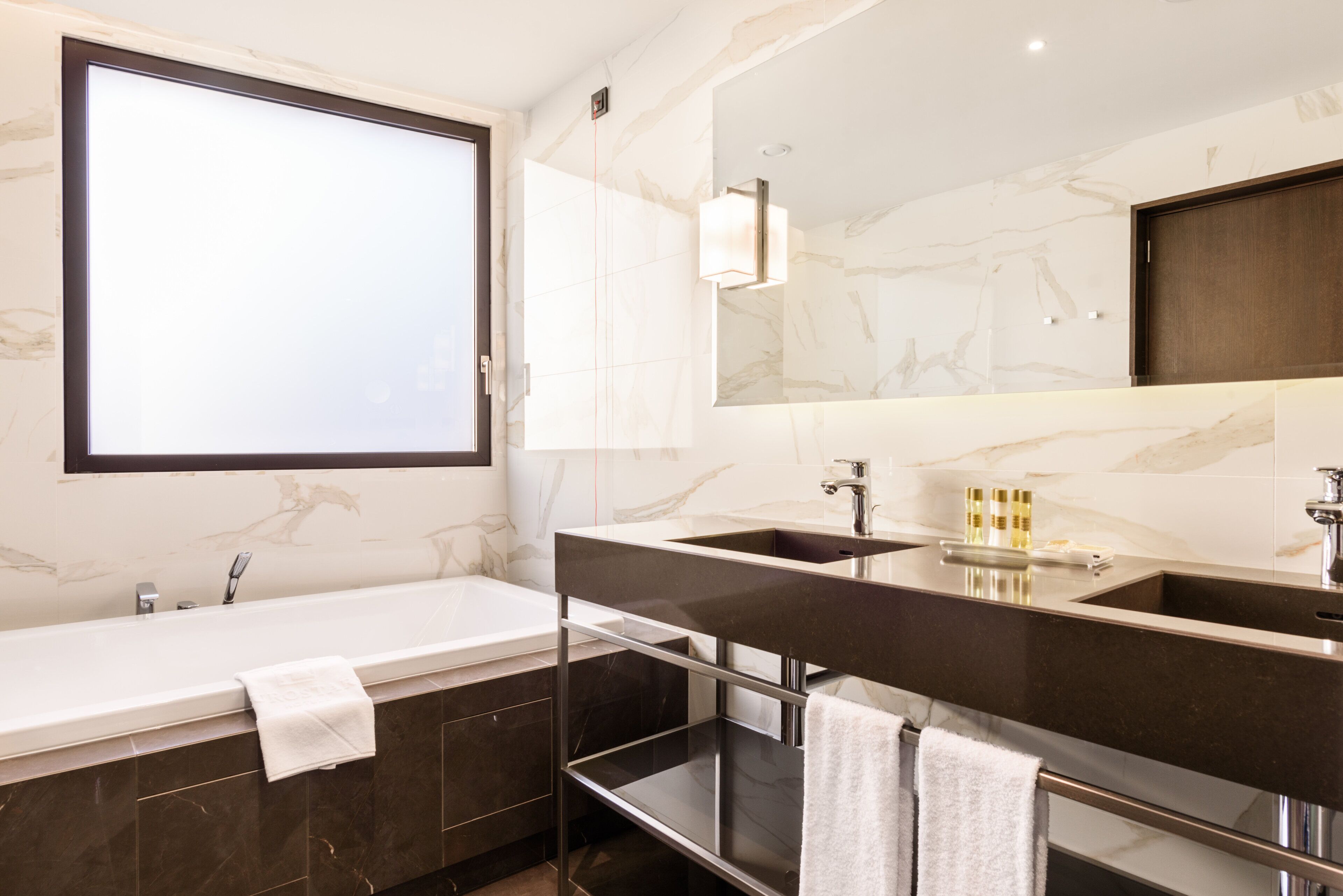 Ein modernes Badezimmer mit großem Spiegel, zwei Waschbecken, einer Badewanne und einem Waschtisch mit Regalen.