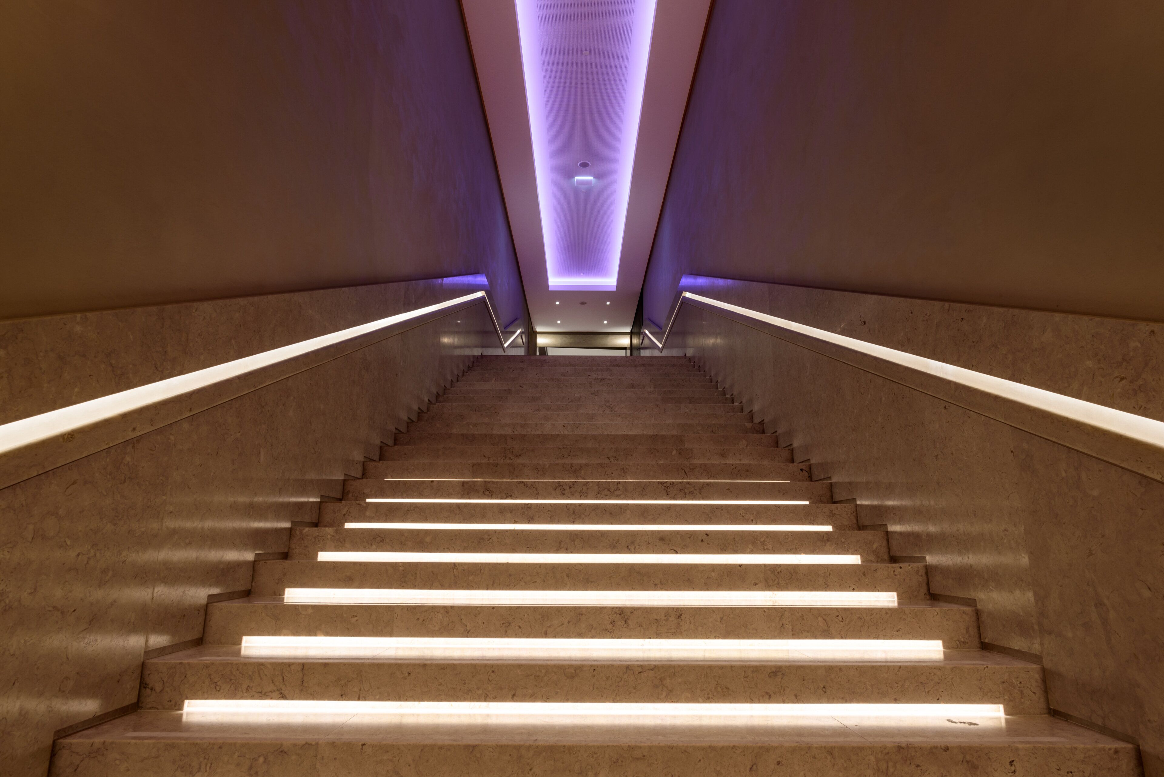 A staircase with illuminated handrails and a purple-lit ceiling.