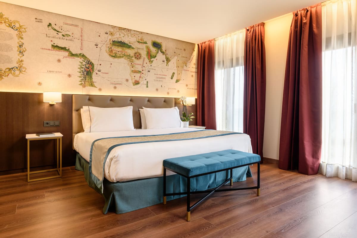 Een netjes ingerichte hotelkamer met een groot bed, een nachtkastje, een kaart aan de muur en een raam met gordijnen.