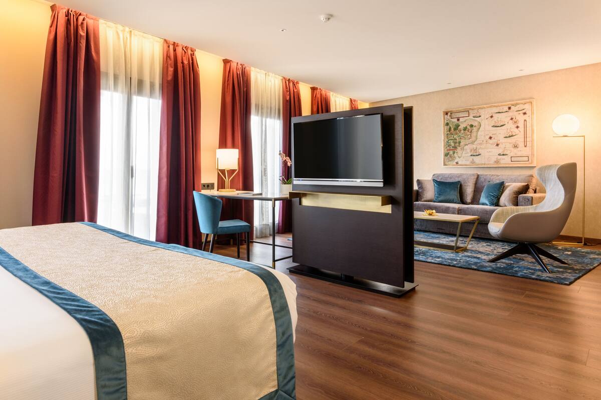 Een hotelkamer met een bed, een televisie, een bureau met stoel, een bank en een kaart aan de muur.