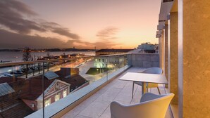 Un balcon donnant sur une vue panoramique de la ville au coucher du soleil, avec une table et des chaises.