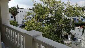 Un balcon donnant sur des bâtiments blancs et un arbre.