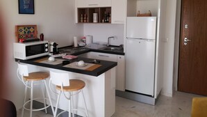 Une cuisine compacte dotée d’un îlot central, de meubles blancs et d’un réfrigérateur.