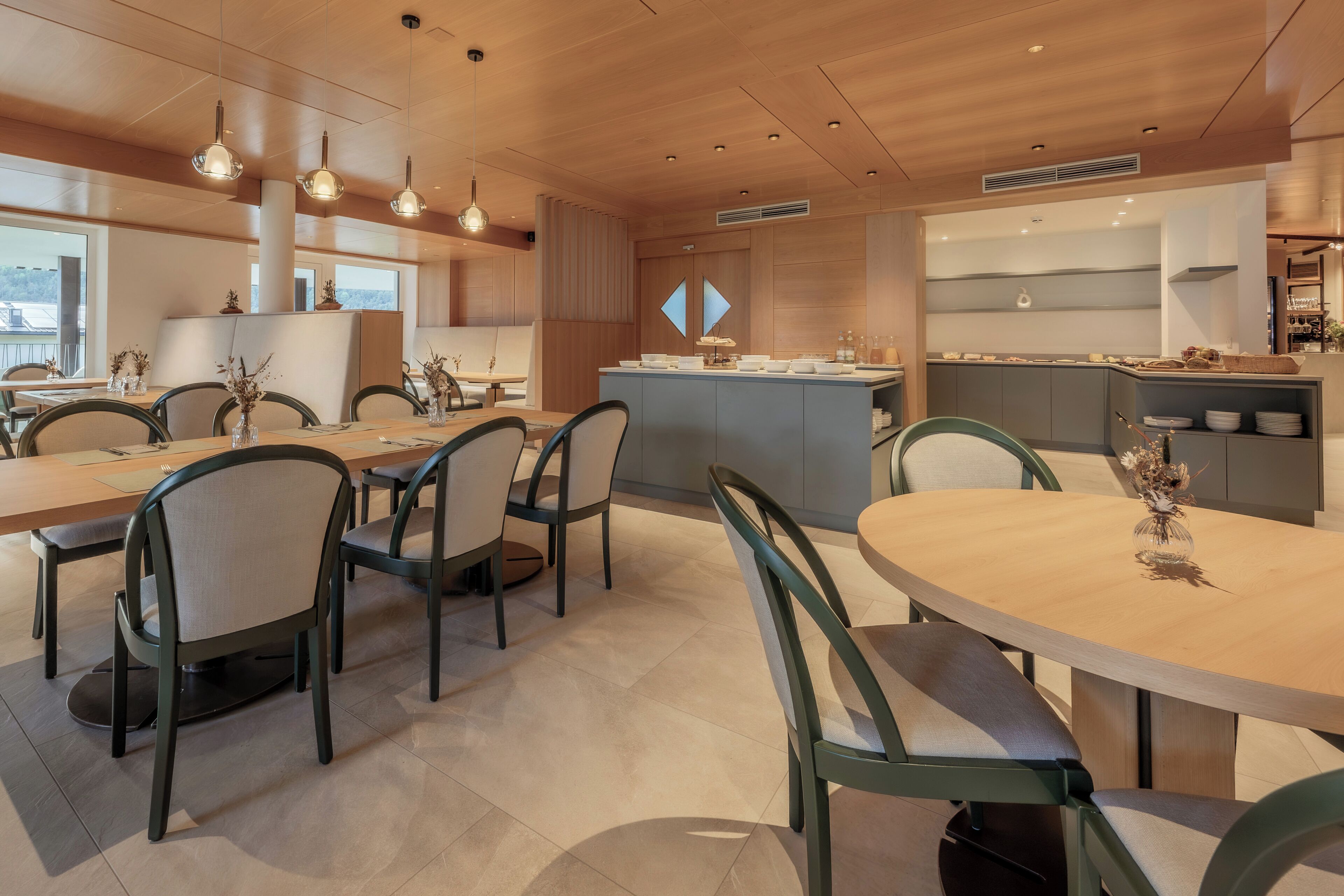 Een moderne eetruimte met houten tafels en stoelen, een centraal eiland met een spoelbak en hangende verlichting.