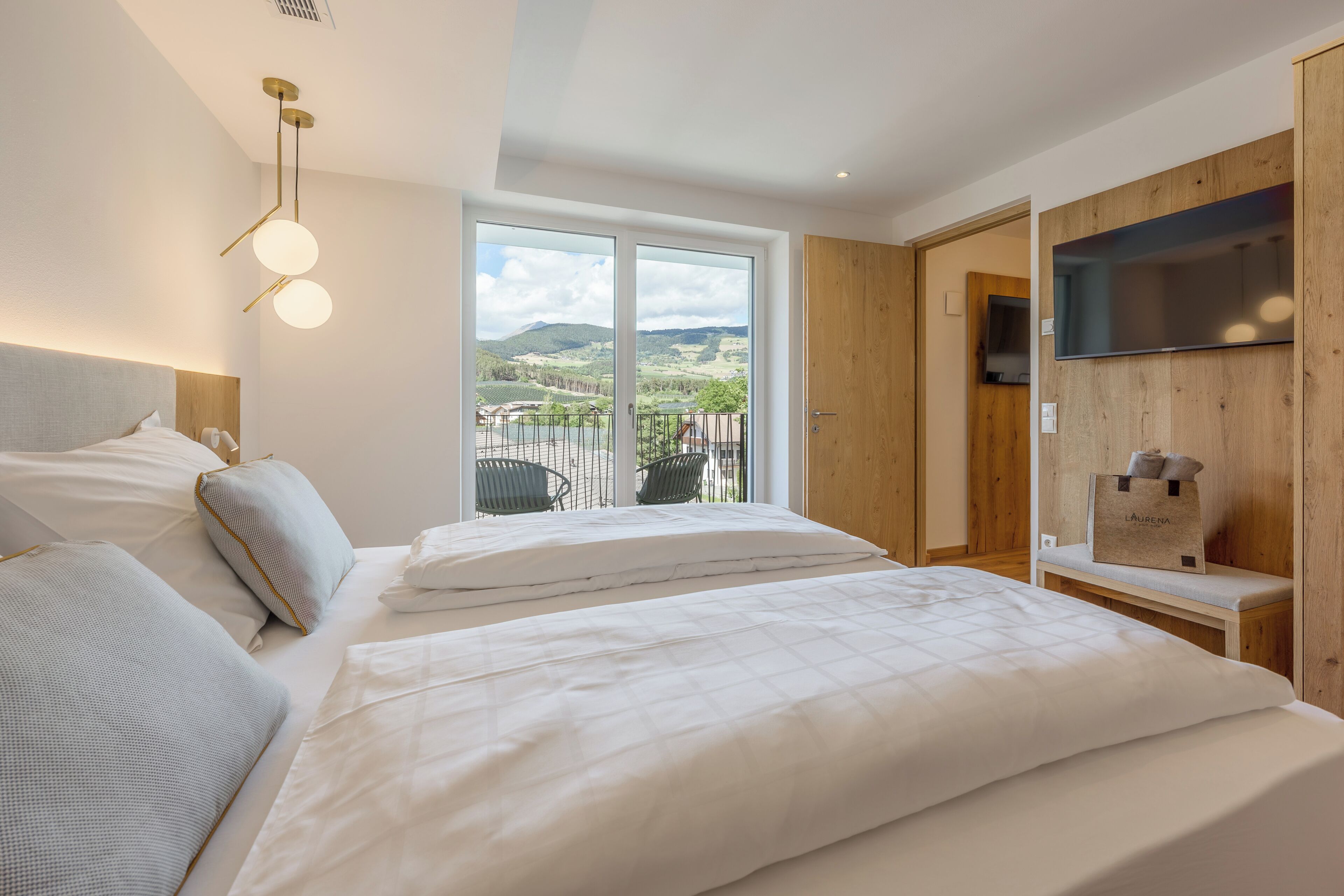 Ein Schlafzimmer mit zwei Betten, einem an einer Holzvertäfelung befestigten Fernseher und einem großen Fenster mit Blick auf Hügel.